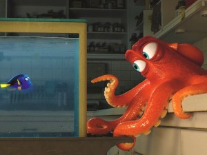 An animated scene from the Pixar film "Finding Dory." In an aquarium, a blue tang fish is in a fishtanks looking at an octopus staring on top of a kitchen counter