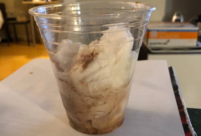 A clear plastic cup filled with tissues soaked with saliva with streaks of brown from something chocolatey.