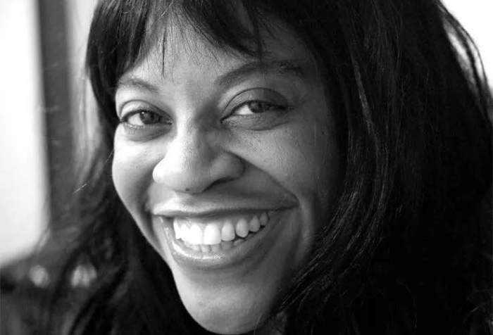 Black and white image of a middle aged African American woman with long hair smiling at the camera.
