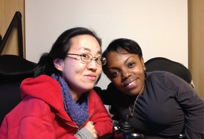 Image of two women in wheelchairs. On the left is an Asian woman with glasses and wearing a red hoodie. On the right is an African American woman with short black hair and a black shirt.