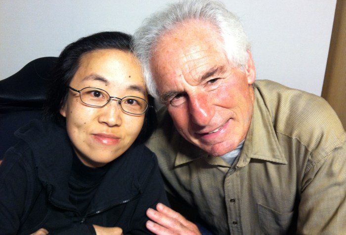 Asian American woman in a black hoodie and in a wheelchair sitting on the left side. Next to her is an older White man with white hair.