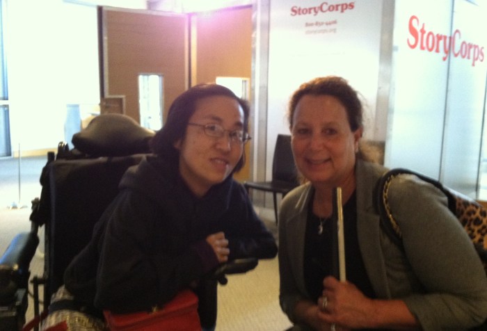Asian American woman in a black hoodie sitting in a wheelchair on the left and on the right is a middle-aged white woman with brown hair pulled back holding a white cane.