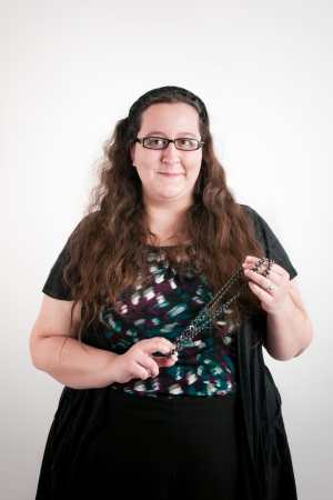 Julia Bascom smiles at the camera. She is a white woman with long brown hair and she is stimming with purple beads in her hands.