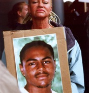 Older black woman with long braids holding a large poster with a photo of her son, a young African American man