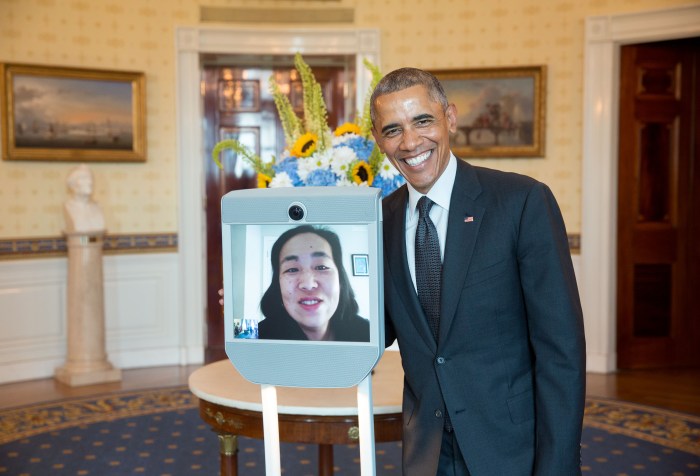 Image of President Barack Obama in the Blue Room of the White House standing next to Alice Wong who is on a screen in a telepresence robot.