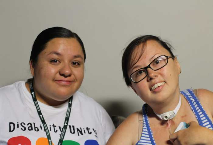 [Left] Dolores is a fat brown femme with a round face. She smiles without showering teeth. Their black hair is pulled back. [Right] Stacey is a mixed race Korean and white queer person wearing a blue-and white striped tank top and her trach can be seen.