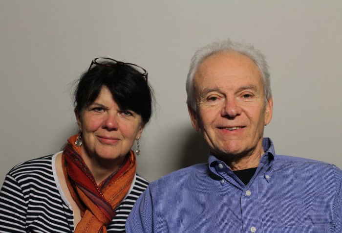 A photo featuring Anthony Tusler and Fran Osborne taken on June 16, 2016: Two people sitting next to each other. The woman on the left is Fran Osborne who appears to be white. She has long dark hair pulled back, with eye glasses on top of her head. She is wearing a black and white striped shirt with an orange scarf tied around her neck. The man on the right is Anthony Tusker who appears to be white. He is wearing a light blue button-down shirt with a black t-shirt inside. He is smiling, and his hair is white and combed back.
