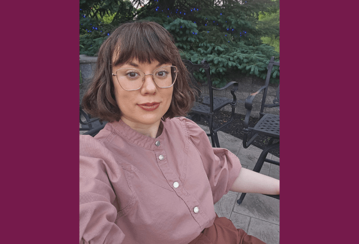 Graphic with a plum colored background. In the center a photo of a young white woman sits outdoors, smiling at the camera. Her brown hair is cut in a long bob with bangs and she has oversized rose-gold glasses. She wears a pink blouse with silver buttons down the front and brown slacks. In the background you can see a patio with iron chairs, and a fir tree lit up with blue lights for the holidays.