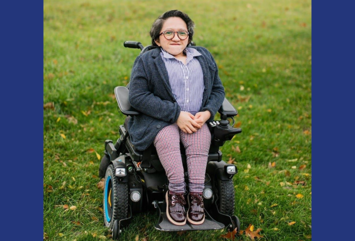 Graphic with a navy blue background featuring a photo of Sandy Ho sitting in her power wheelchair in the middle of a field of green grass, with houses blurred in the background. She has short dark wavy hair and tortoise shell glasses on. Sandy is wearing maroon shoes, plaid pants, a dark gray cardigan, and a button-up blue and white striped collar shirt. She is smiling at the camera with her hands in her lap.
