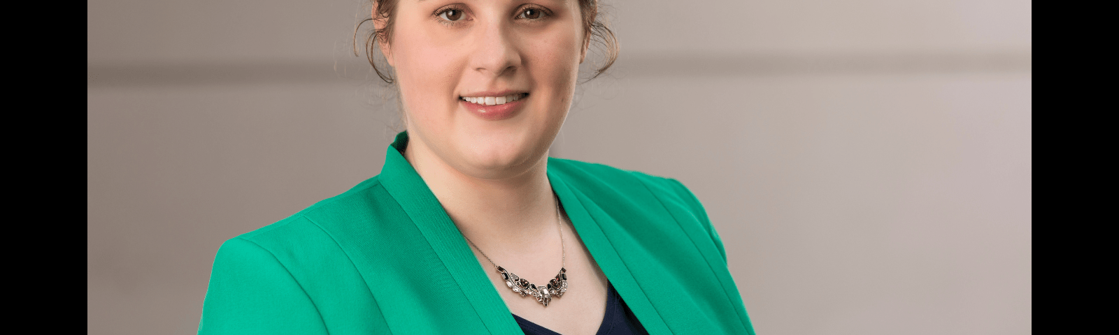 Sarah, a white woman with brown hair pulled back, smiling at the camera. She is wearing a green blazer and navy blouse.