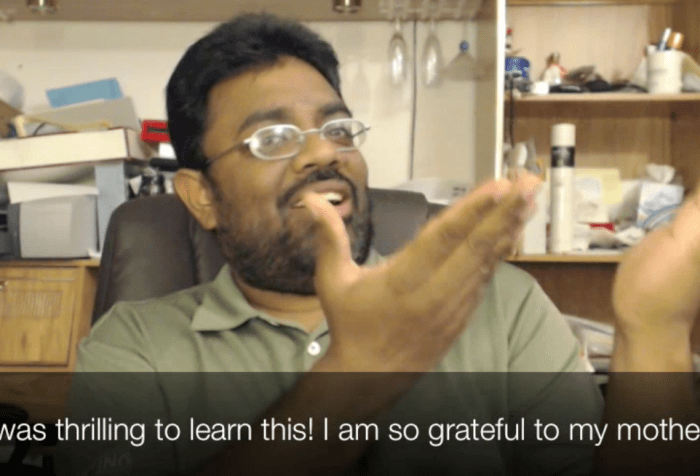 A South Asian Indian man with glasses and a beard is signing in sign language with his two hands raised. The caption reads: "It was thrilling to learn this! I am so grateful to my mother!"
